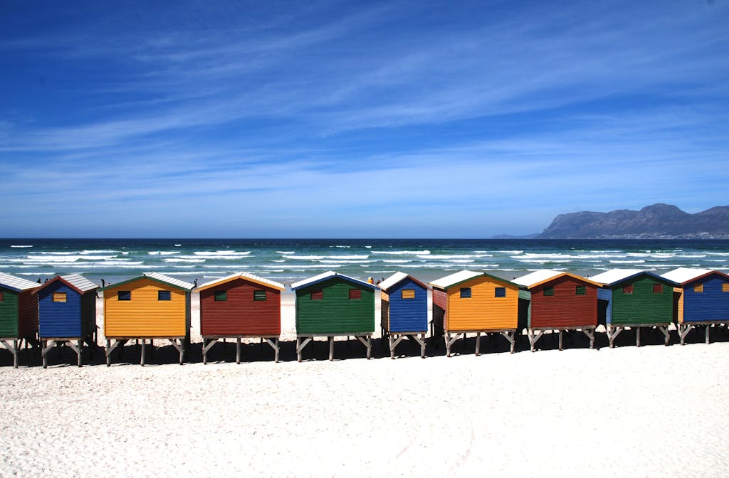 Colorful beach huts on a sunny seaside with scenic ocean views and mountains.