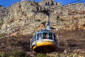 A cable car carries tourists up Table Mountain in Cape Town, showcasing the rocky cliff face.